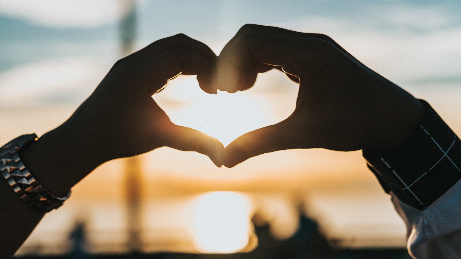 Hands held together to make the shape of a heart with a sunset in the background.