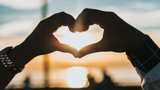 Hands held together to make the shape of a heart with a sunset in the background.