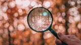 A magnifying glass held up to an autumnal coloured woodland.