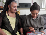 Shared Lives carer, Lorna, sat on the sofa with Summa. They are looking at an ipad. 