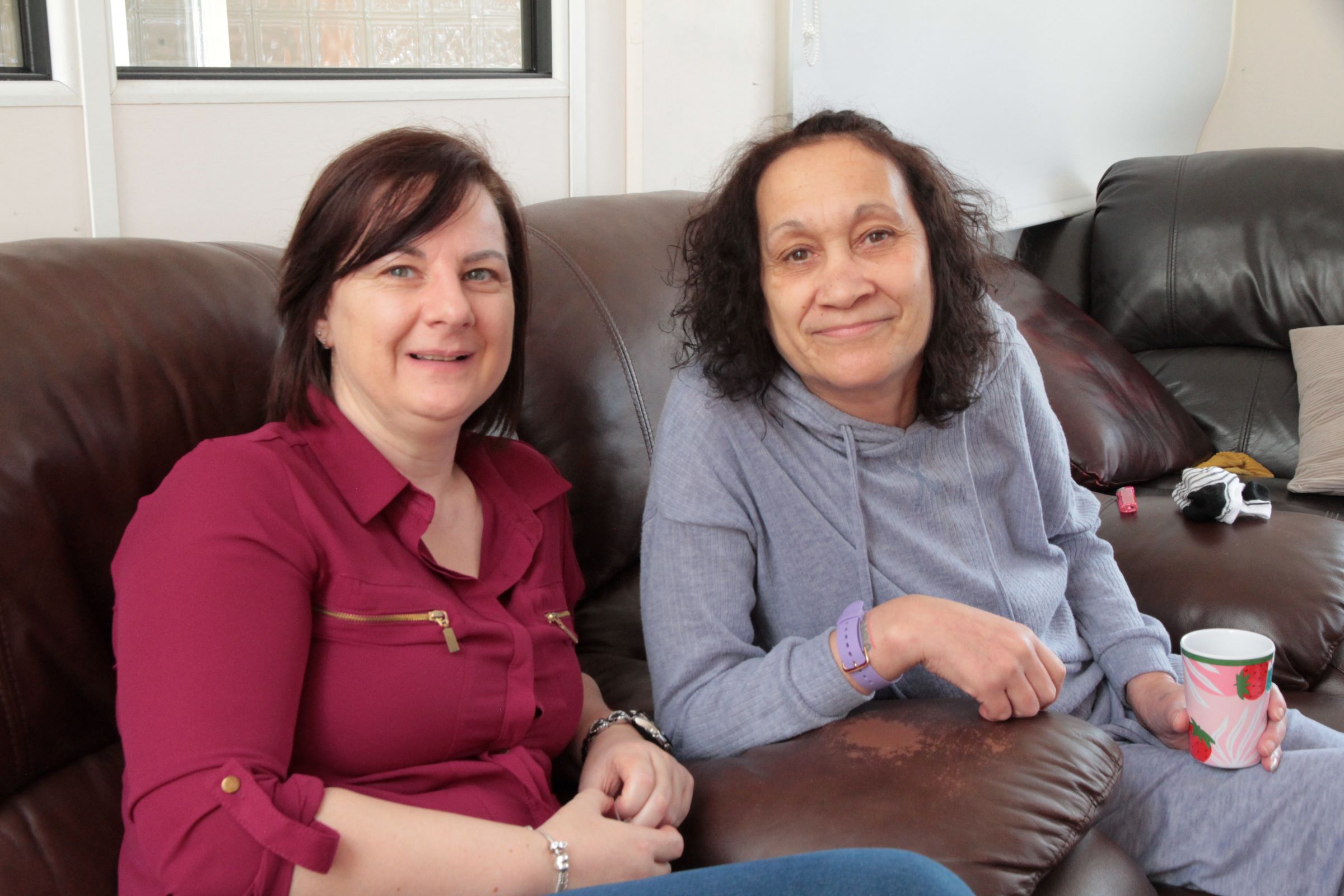 Two women smiling while sat on the sofa together