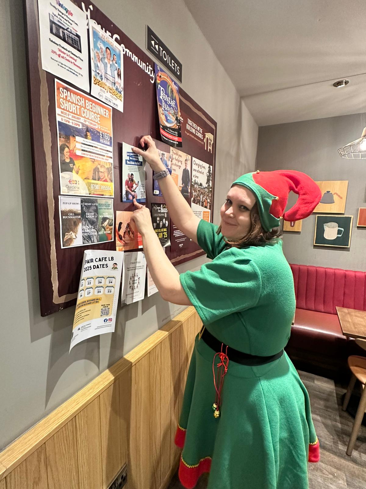 Clare putting up posters dressed as a Christmas elf