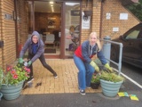 Two women leaning down showing the plants that have just been potted at the entrance to the building