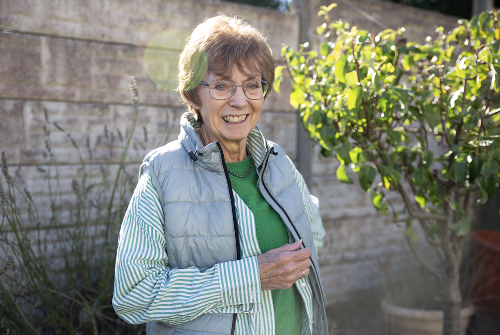 An older woman standing in a garden smiling