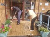 A man and a woman sweeping the entrance to a brick building