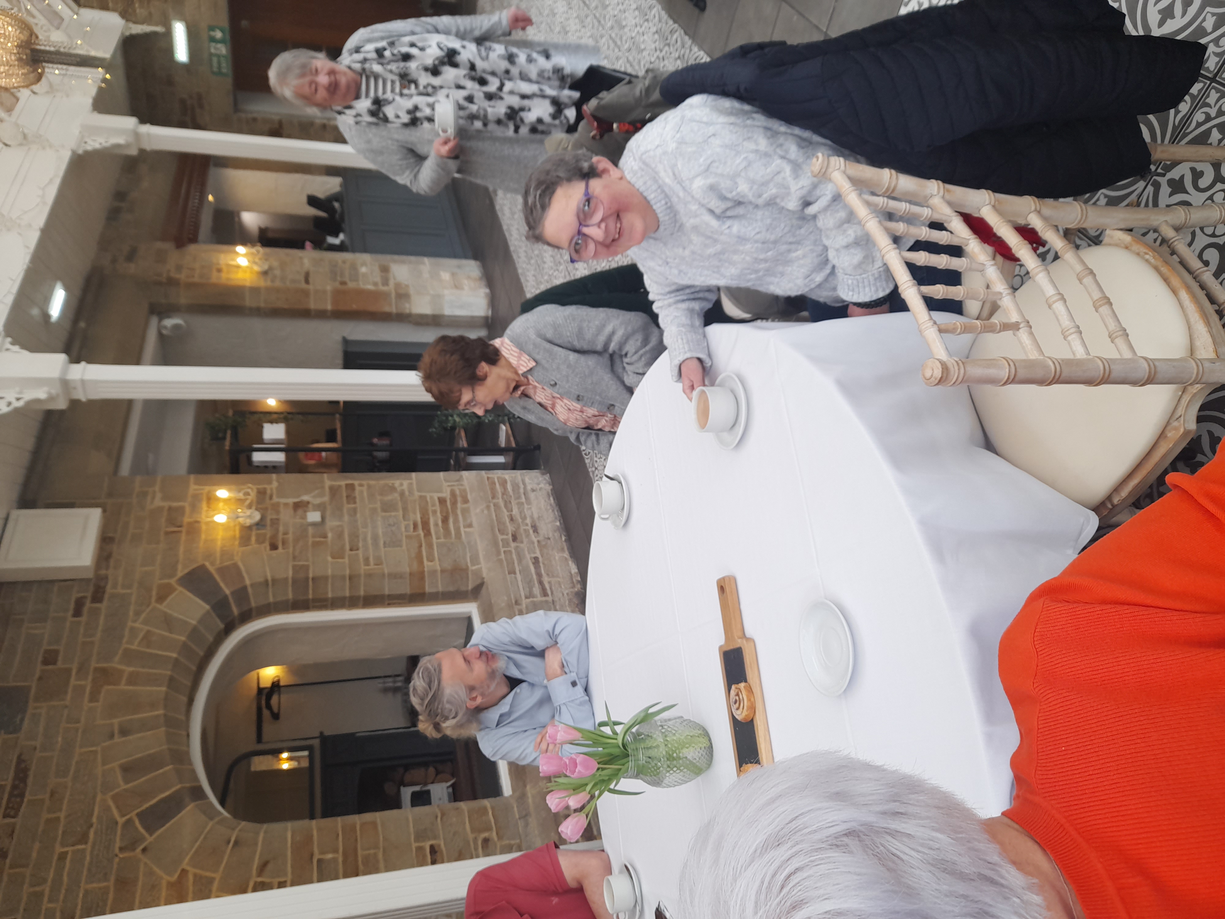 One man and two ladies sat down having tea, one lady behind them.