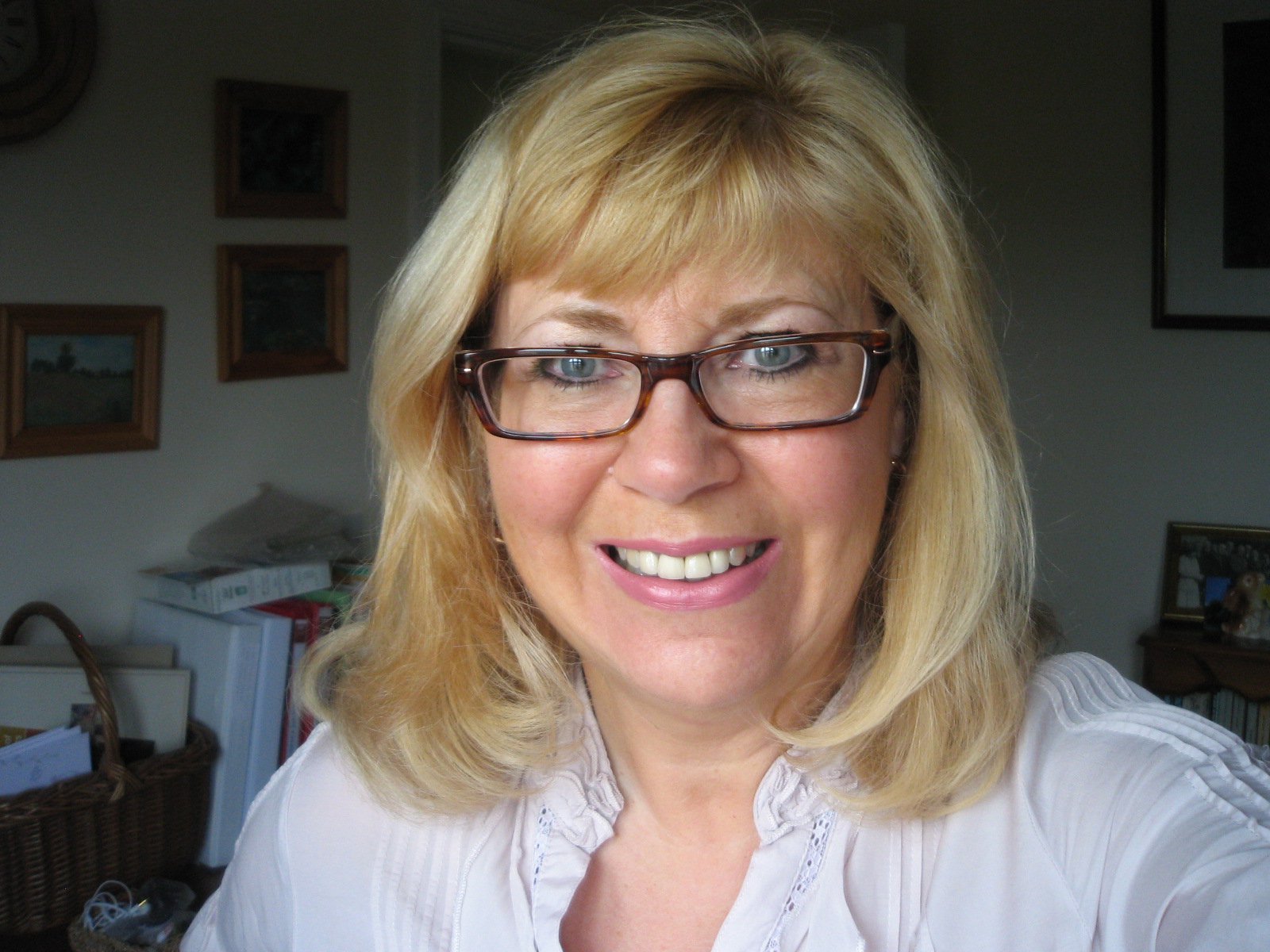 A lady with blonde hair and glasses smiling at camera.