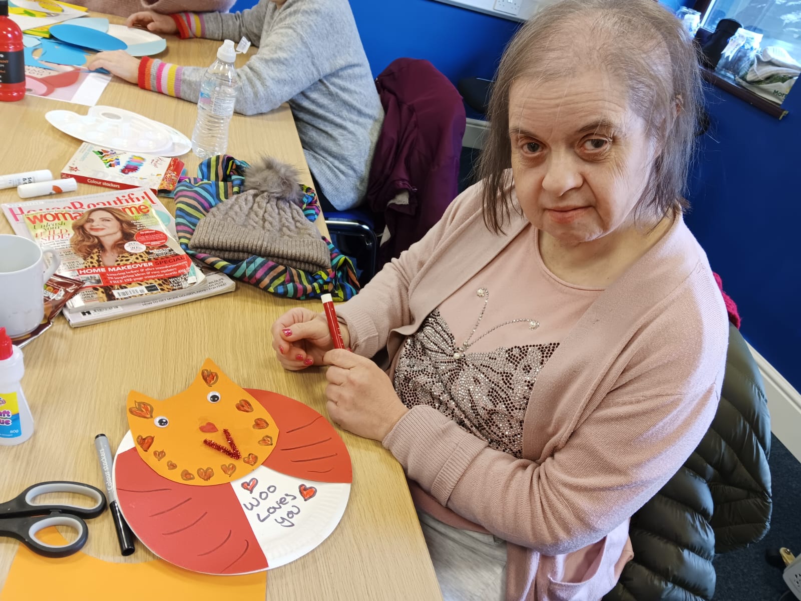 Miriam looking at the camera with her completed valentines day owl. Which has an orange face and a red body.