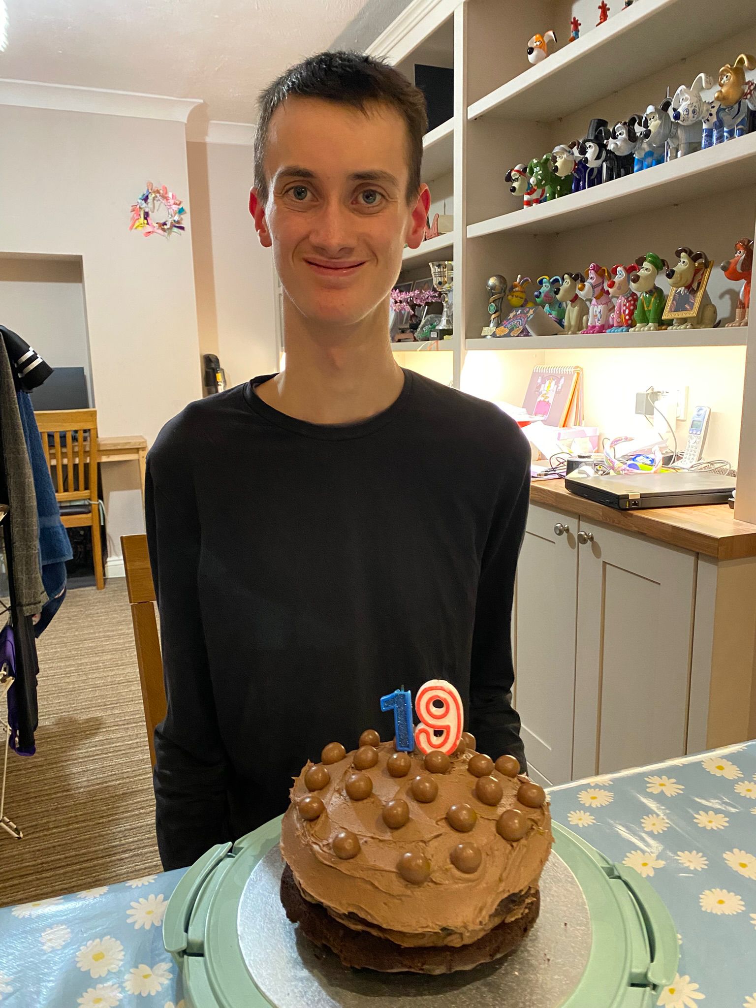 Nathan smiling at the camera with his birthday cake in front of him, it has the candles for 19 on top.