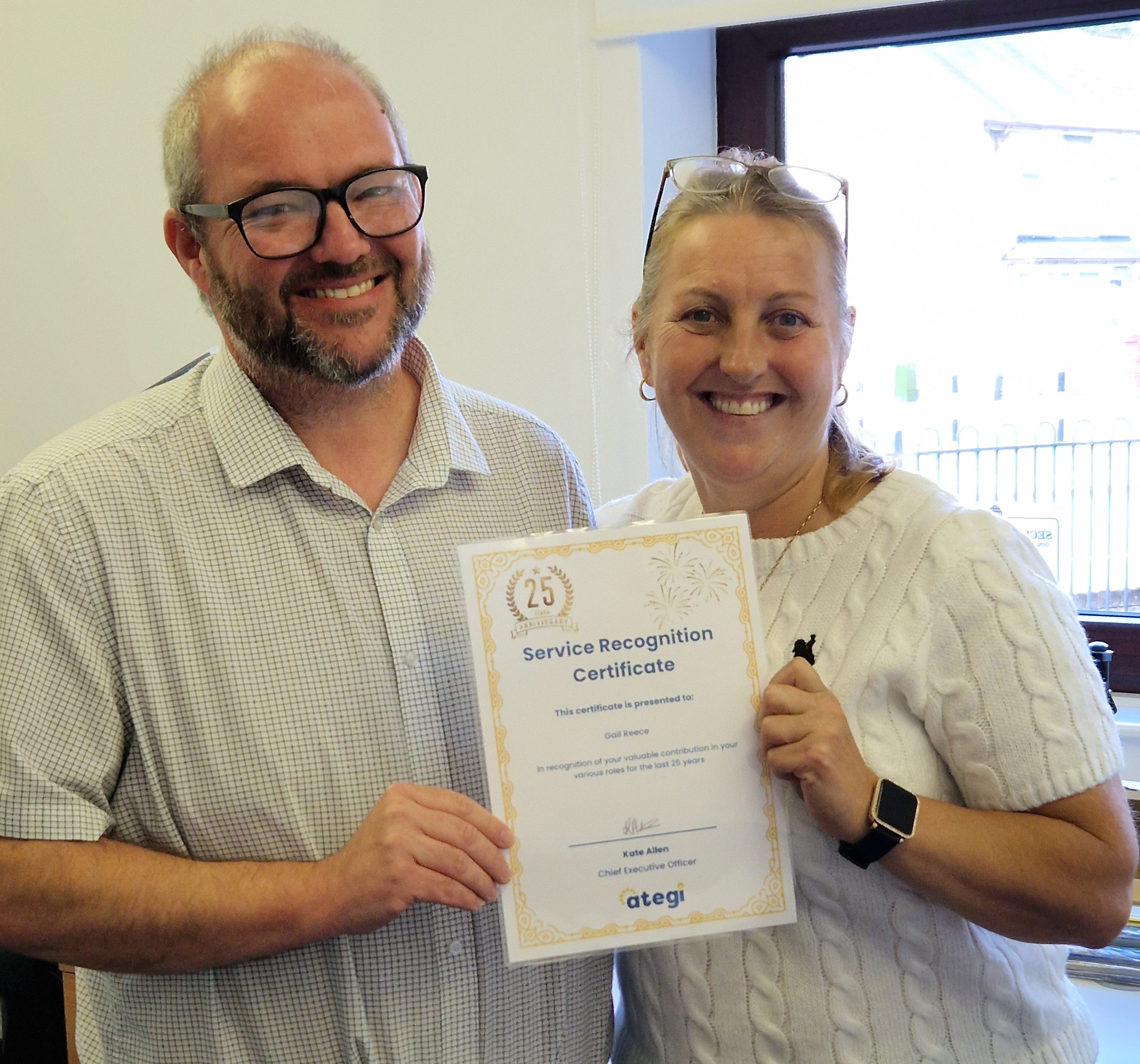 Gail and Richard smiling at camera holding a certificate of service recognition.