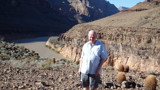 An older bald man stood in a rocky barren landscape. A desert probably.